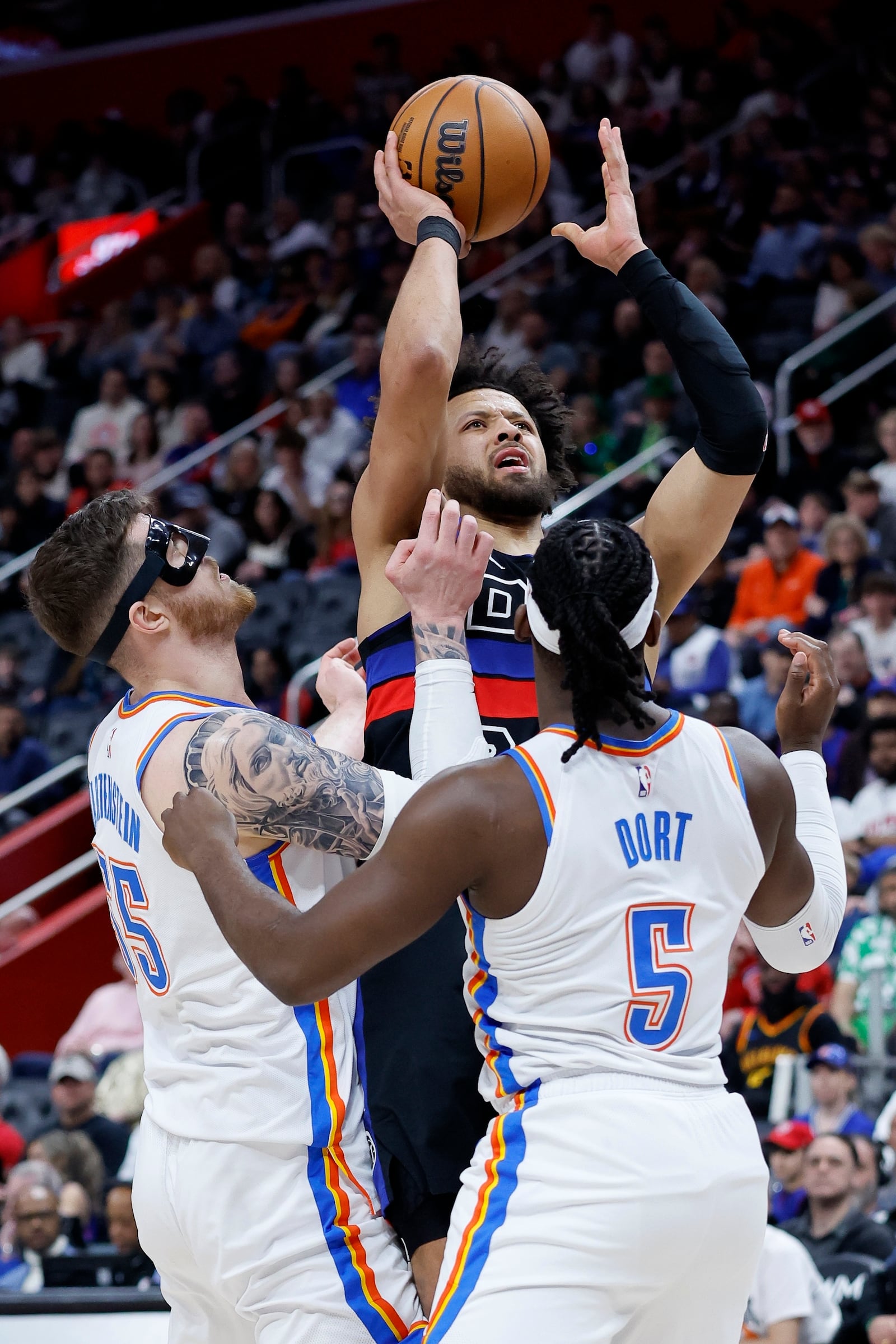 Detroit Pistons guard Cade Cunningham, top, looks to shoot against Oklahoma City Thunder center Isaiah Hartenstein, left, and guard Luguentz Dort (5) during the first half of an NBA basketball game Saturday, March 15, 2025, in Detroit. (AP Photo/Duane Burleson)