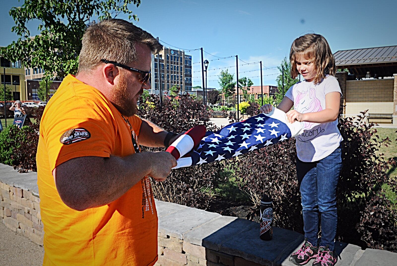 Amber Hillis, 5, helps her father Tyson case the flag after watching the Jeep parade Thursday, July 19, 2018, at Austin Landing.  More than 100 Wounded Warriors and Gold Star families took part in the event. (Marshall Gorby/Staff)