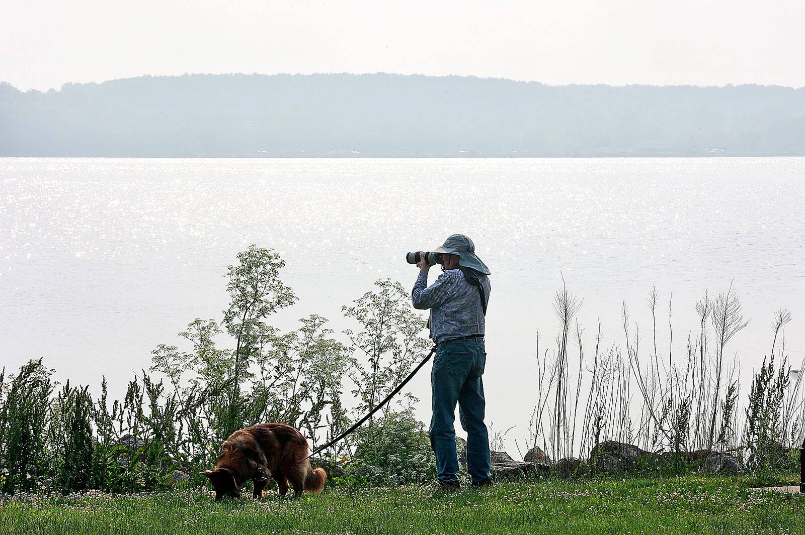 Dan Kempf stops to take a picture of the hazy air at C.J. Brown Reservoir created by the wildfires in Canada as he walks along the shoreline with his dog, Tika, Tuesday, June 6, 2023. The smoke was so thick that it obscured the shore on the other side of the lake. BILL LACKEY/STAFF