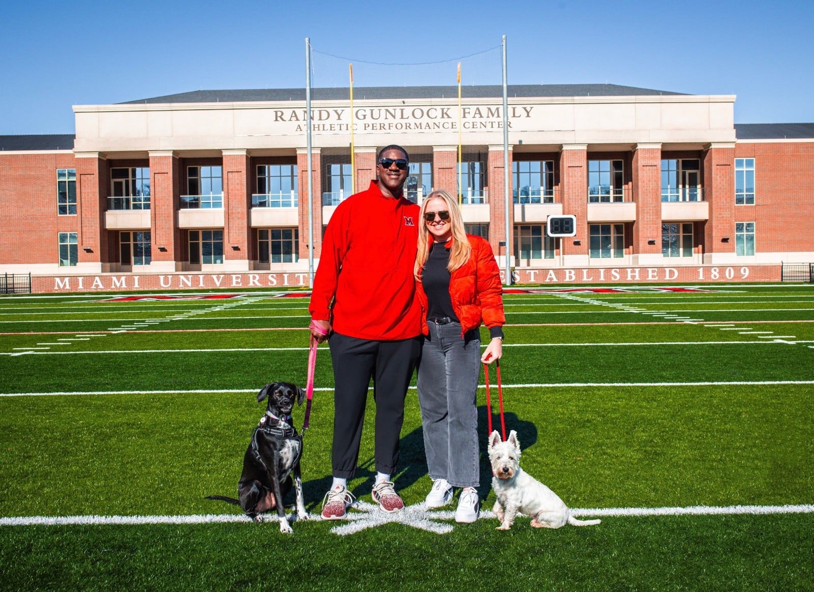 Chris and Catherine Hudson on the football field at Yager Stadium with their two dogs, Callie (left) and Chief. CONTRIBUTED