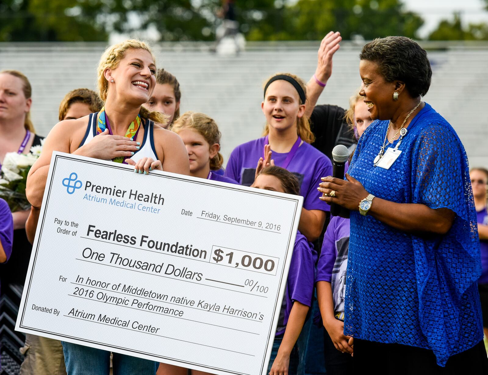 Anita Scott Jones presented a check from Atrium Medical Center to two-time Olympic Gold Medalist in Judo Kayla Harrison for her Fearless Foundation during a pre-game ceremony before the Middies game Friday, Sept. 9 in Middletown. NICK GRAHAM/STAFF