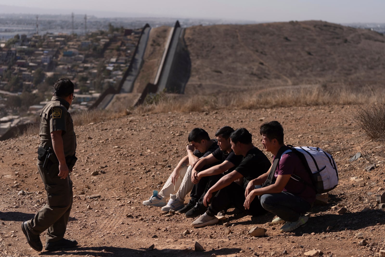 Border Patrol Agent Gutierrez walks past four men detained after crossing the border illegally in a gap in two walls separating Mexico from the United States before turning themselves in, Thursday, Jan. 23, 2025, in San Diego. (AP Photo/Gregory Bull)