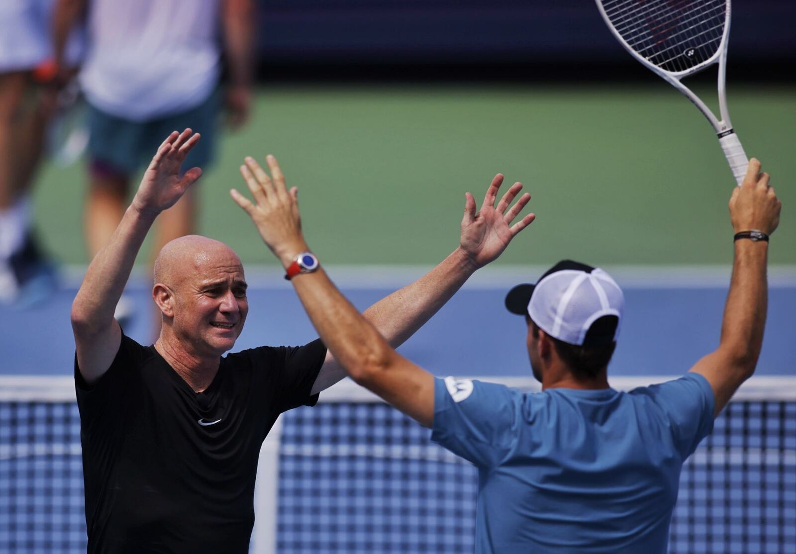 Andre Agassi, left, celebrates with partner Tommy Paul after winning an exhibition match against John Isner and Andy Roddick during Community Day to kick off the Cincinnati Open tennis tournament Saturday, Aug. 10, 2024 at Lindner Family Tennis Center in Mason. NICK GRAHAM/STAFF