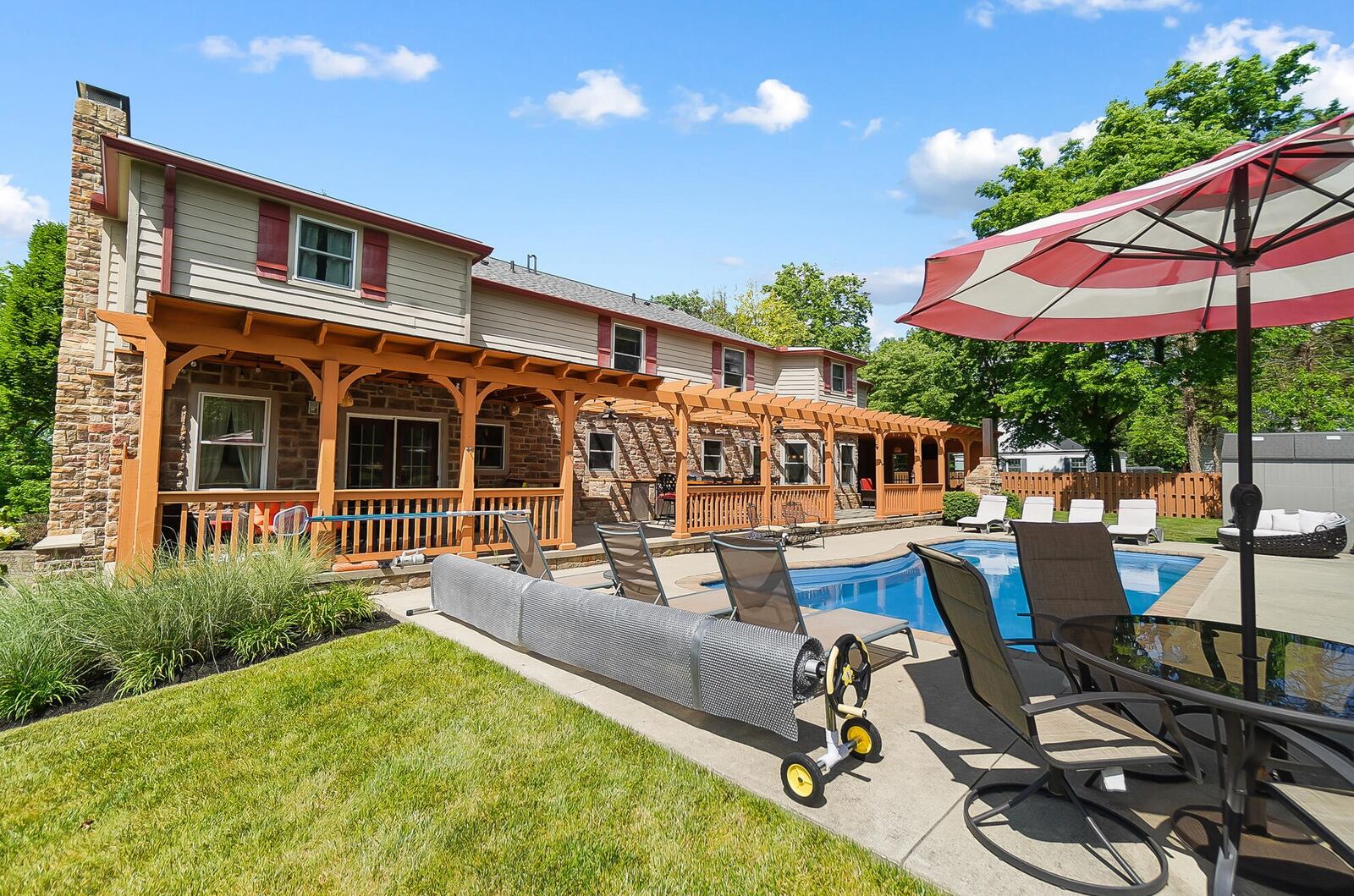 The rear of the home features a wood pergola across most of the back with wood railings, outdoor kitchen, inground pool, outdoor fireplace and wood fence.