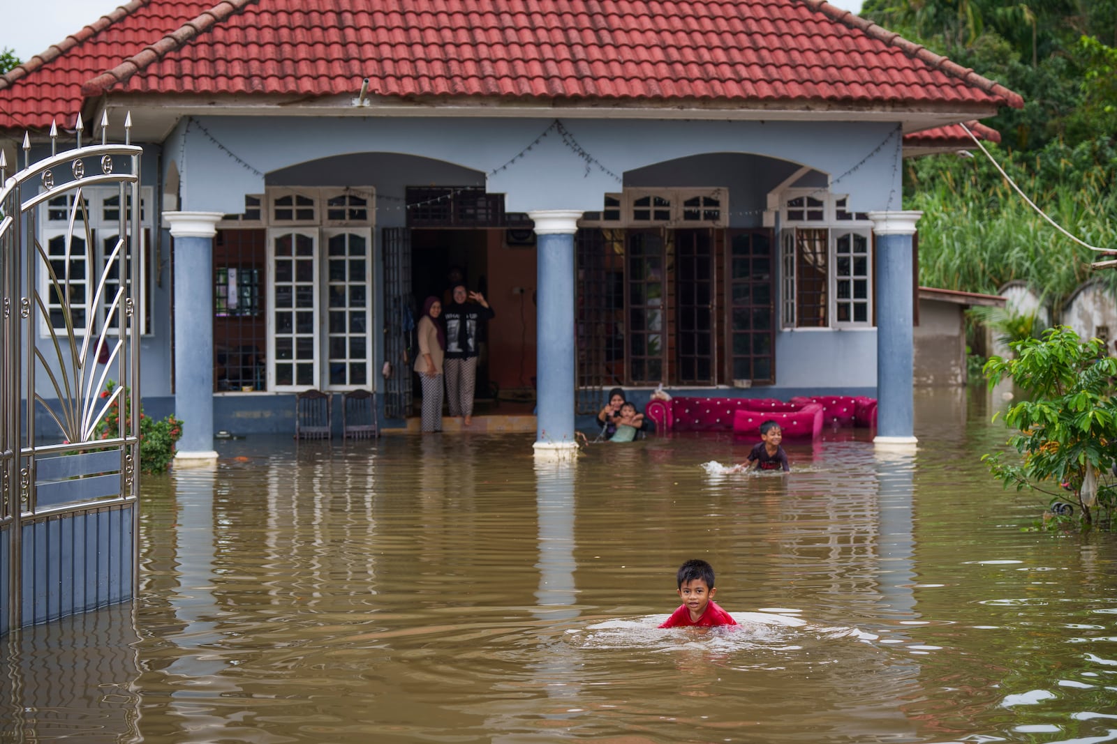 Children wade through flood water outside their home in Tumpat, outskirts of Kota Bahru, Malaysia, Tuesday, Dec. 3, 2024. (AP Photo/Vincent Thian)