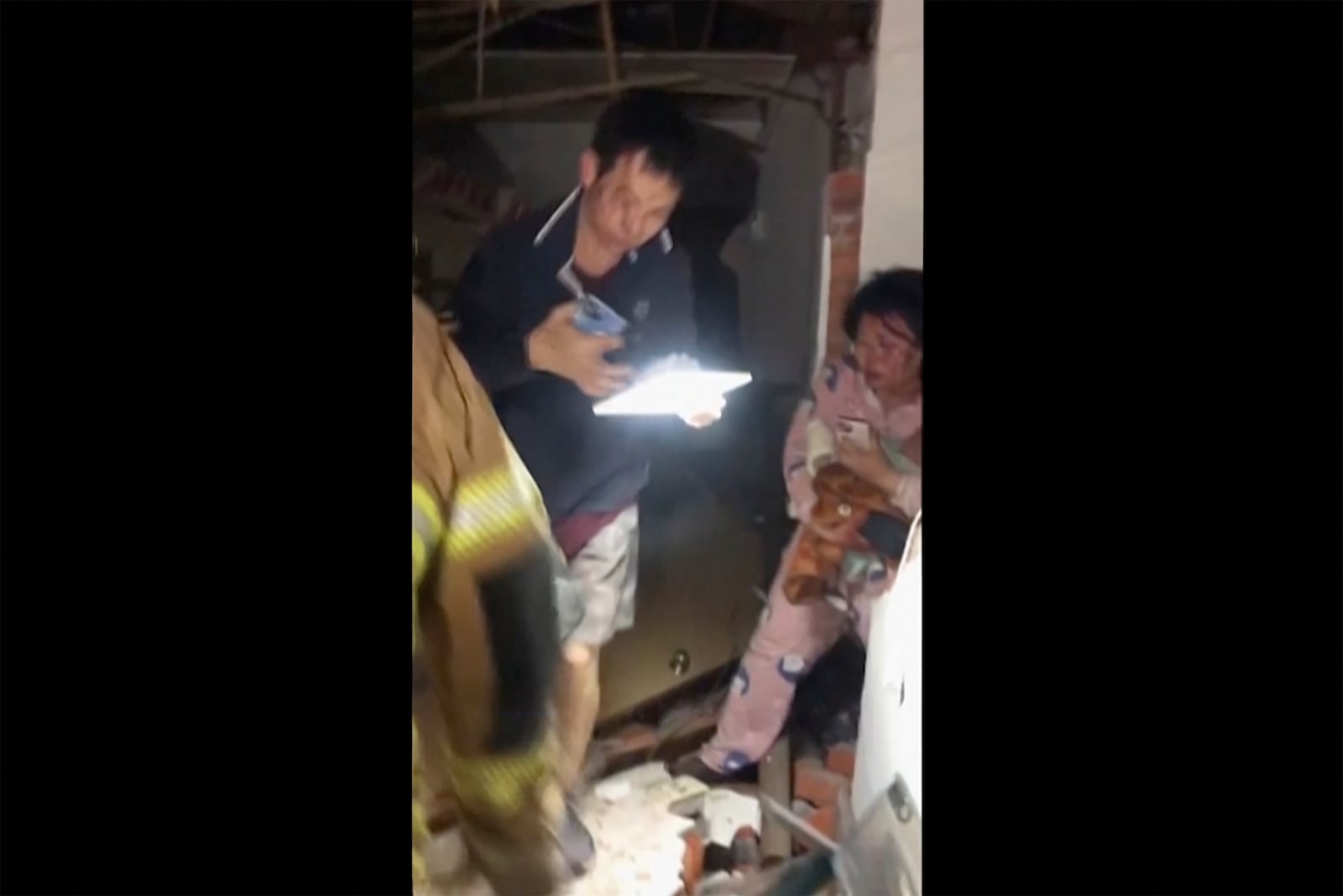 In this image from a video released by Tainan City Government Fire Bureau, firefighters, partially seen at left, help the injured residents, center and right, move out of a damaged house in Tainan, Taiwan Tuesday, Jan. 21, 2025, after an earthquake. (Tainan City Government Fire Bureau via AP)