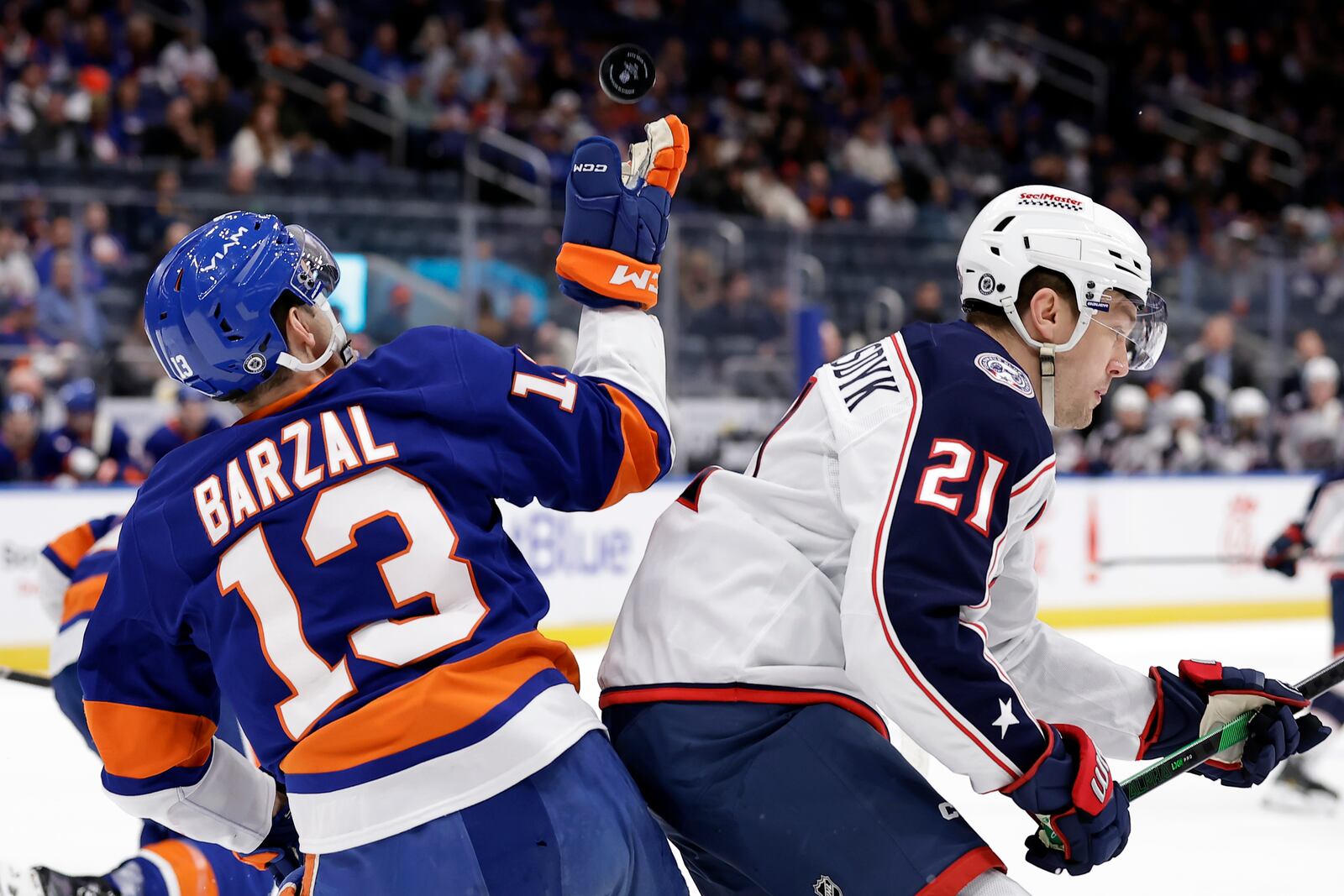 New York Islanders center Mathew Barzal (13) reaches for a puck behind Columbus Blue Jackets left wing James van Riemsdyk, right, in the first period of an NHL hockey game Monday, Jan. 20, 2025, in Elmont, N.Y. (AP Photo/Adam Hunger)