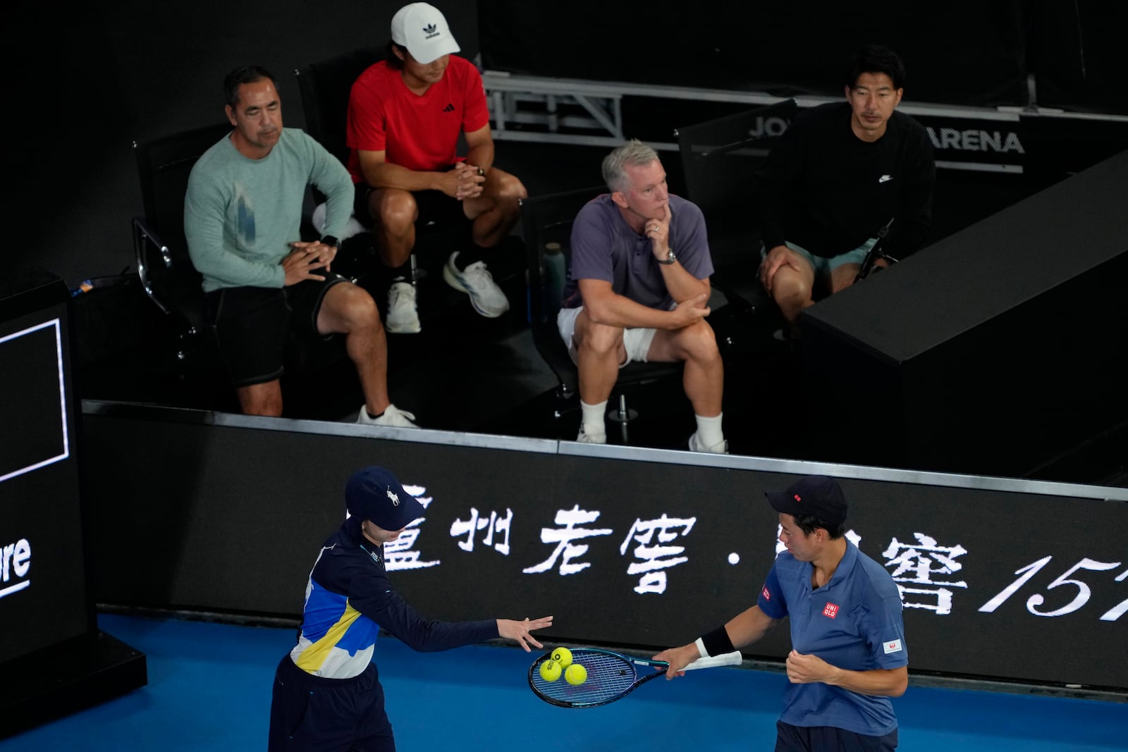 Coaching team for Kei Nishikori of Japan watch as a ball kid gives tennis balls to Nishikori during his first round match against Thiago Monteiro of Brazil at the Australian Open tennis championship in Melbourne, Australia, Sunday, Jan. 12, 2025. (AP Photo/Ng Han Guan)