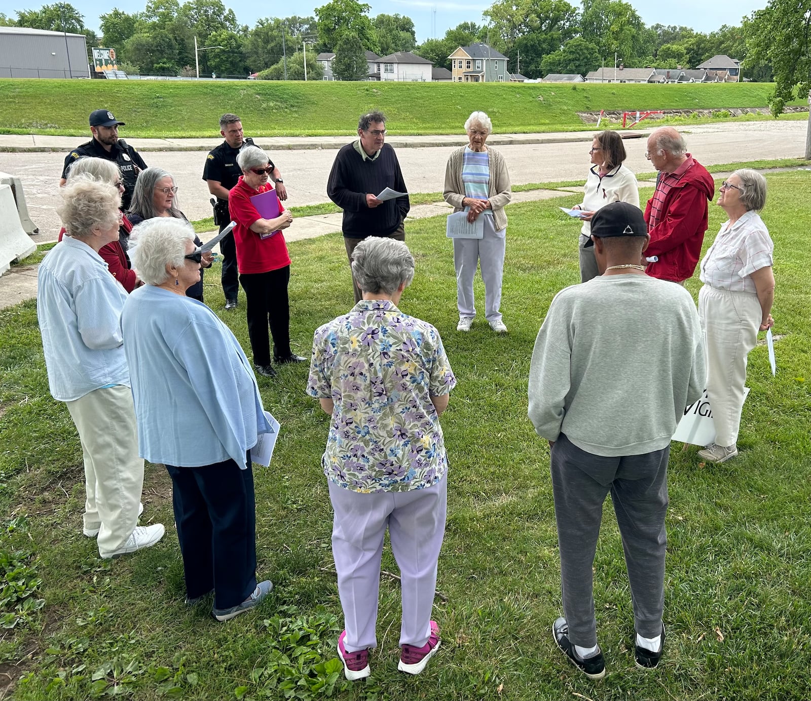 Two Dayton police officers join a group of Dayton-area residents holding a prayer vigil for homicide victims June 8, 2024, at McIntosh/Riverview Park in Dayton. JEREMY P. KELLEY / STAFF