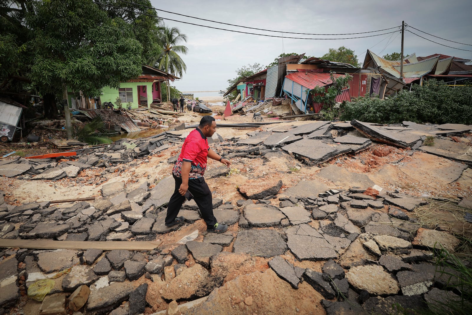 A resident crosses a road past houses damaged by flood in Tumpat, outskirts of Kota Bahru, Malaysia, Tuesday, Dec. 3, 2024. (AP Photo/Vincent Thian)