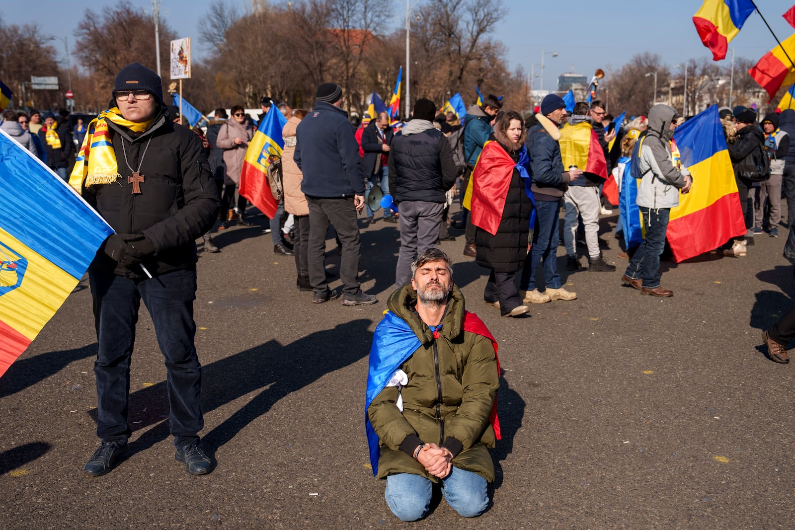 A man prays while kneeling during a protest by supporters of Calin Georgescu, the winner of Romania's first round of presidential election which the Constitutional Court later annulled, in Bucharest, Romania, Monday, Feb. 10, 2025. (AP Photo/Vadim Ghirda)