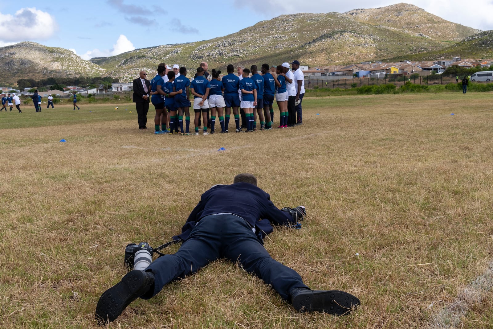 A photographer lies on the ground to take a picture of Britain's Prince William greeting pupils at the Ocean View Secondary School in Cape Town, South Africa, Monday, Nov. 4, 2024. (AP Photo/Jerome Delay-pool)