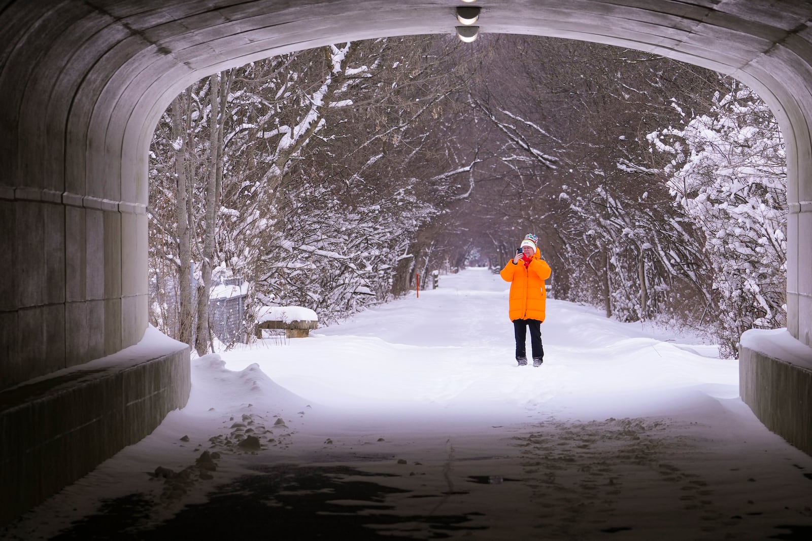 A walker pauses to take a photo as she walks along the snow-covered Monon Trail in Carmel, Ind., Monday, Jan. 6, 2025. (AP Photo/Michael Conroy)