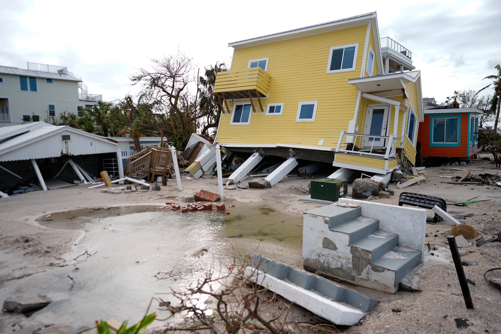 A house, center, lies toppled off its stilts after the passage of Hurricane Milton, alongside an empty lot where a home was swept away by Hurricane Helen, in Bradenton Beach on Anna Maria Island, Fla., Thursday, Oct. 10, 2024. (AP Photo/Rebecca Blackwell)