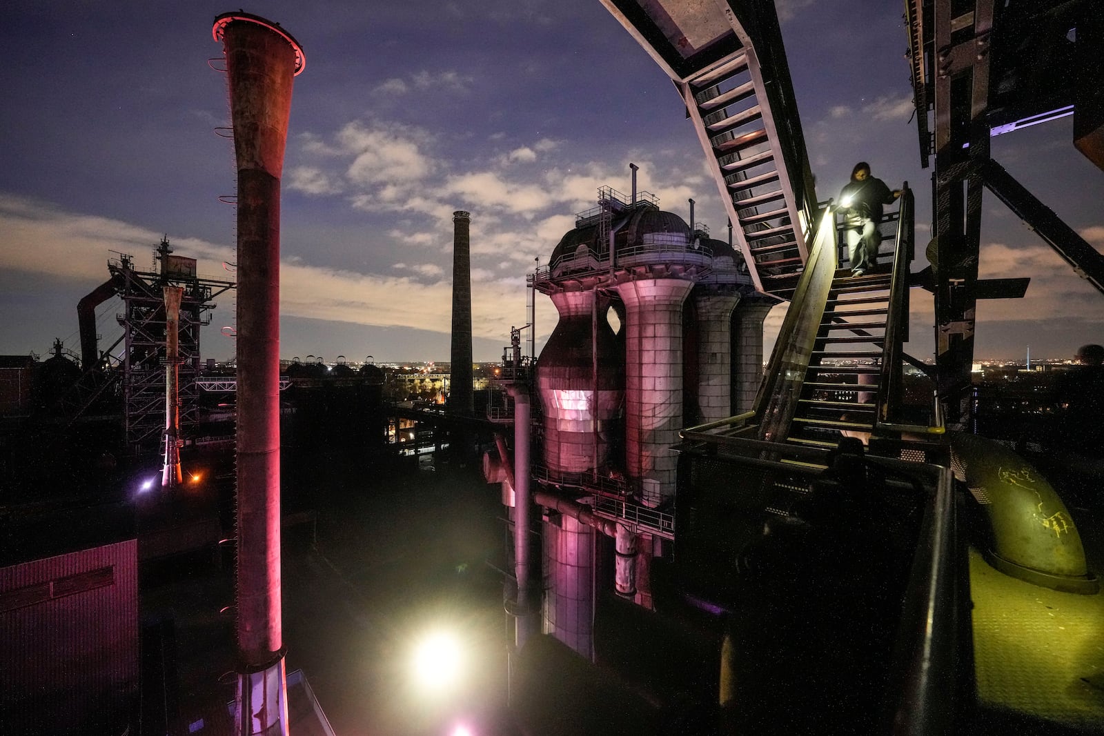 FILE - Young people with flashlights climb down stairs from an old blast furnace of a former steel factory, which has become an industrial landmark and meeting place for teenagers in the evening, 40 years after the last steel was cooked in the old Thyssen factory in Duisburg, Germany, Monday, Jan. 27, 2025. (AP Photo/Martin Meissner, File)