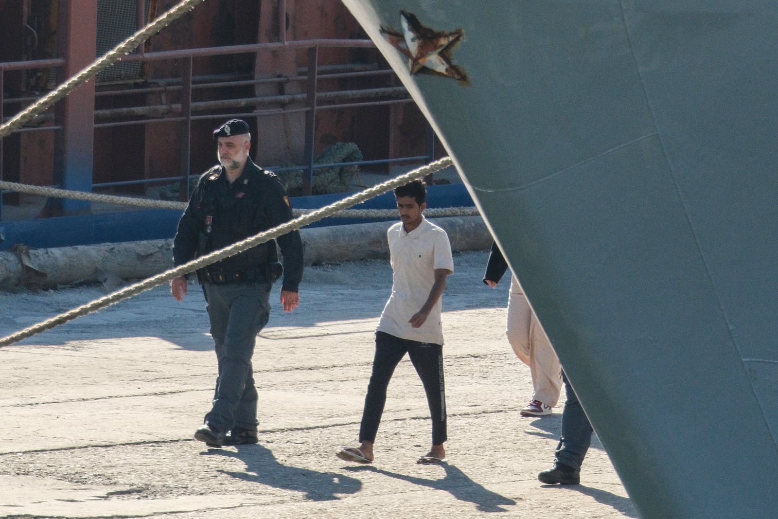 A migrant and security officials walk at the port of Shengjin, northwestern Albania. Wednesday, Oct. 16, 2024 after disembarking from the Italian navy ship Libra, carrying the first group of 16 migrants intercepted in international waters. (AP Photo/Vlasov Sulaj)