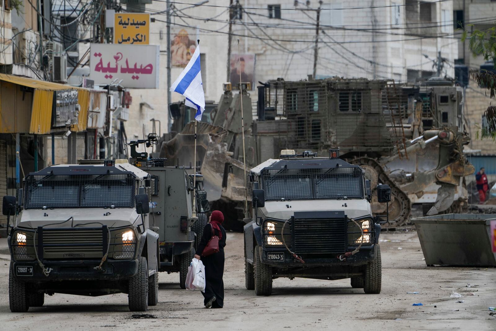 Israeli military vehicles guard a road where a military bulldozer operates in the West Bank refugee camp of Jenin Wednesday, Jan. 22, 2025. (AP Photo/Majdi Mohammed)