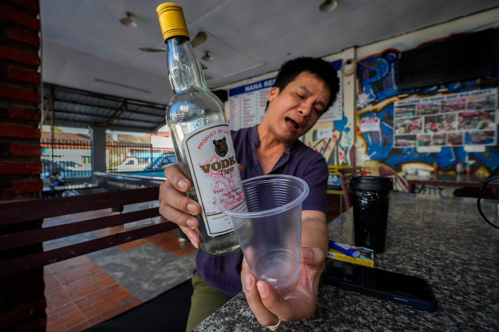 Duong Duc Toan, the manager of Nana Backpack hostel displays a bottle of vodka, in the bar of the hostel in Vang Vieng, Laos, Tuesday, Nov. 19, 2024. (AP Photo/Anupam Nath)