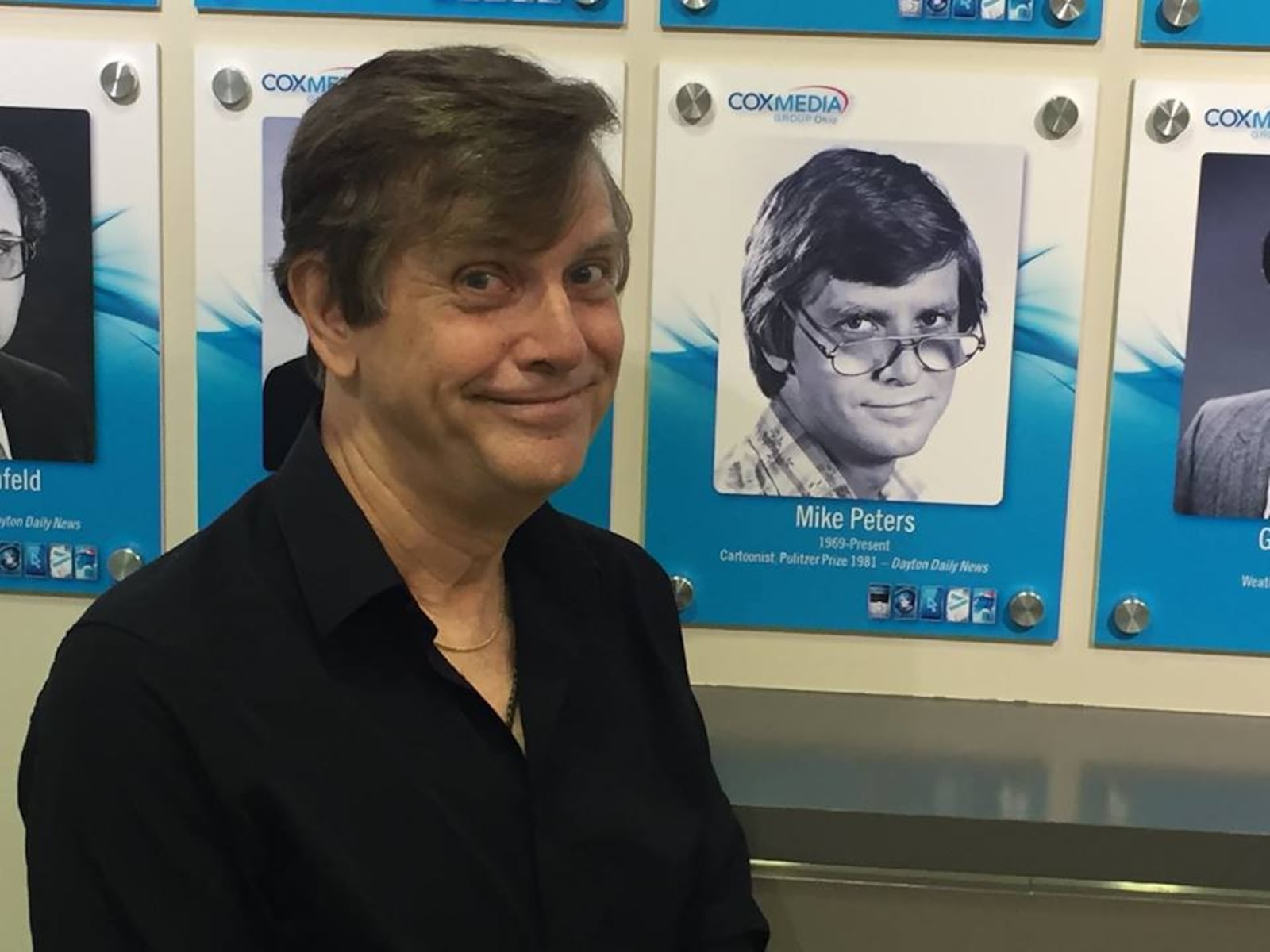 Pulitzer prize winning editorial cartoonist Mike Peters  stands in front on his photo in the Cox Media Group Ohio wall of dame.