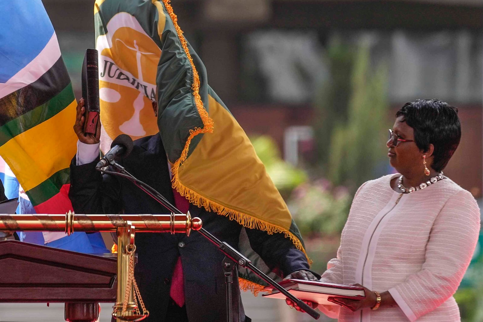 Kenya's new Deputy President Kithure Kindiki, center, is covered by a waving flag as his wife Joyce Kithure, right, holds the Bible at a swearing in ceremony held at Kenyatta International Convention Centre, in Nairobi, Kenya Friday, Nov. 1, 2024. (AP Photo/Brian Inganga)