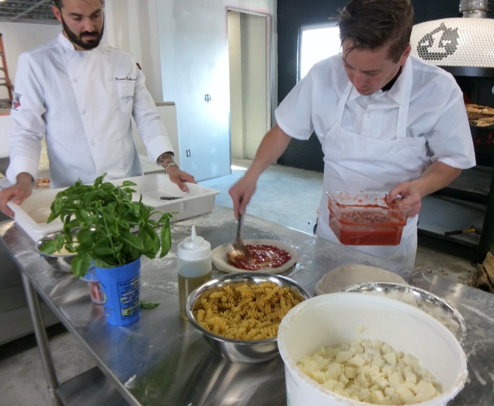 Old Scratch Pizza Kitchen Manager Nate Vance makes a pizza under the watchful eye of Gianni Gallucci, left, a member of the Associazione Pizzaiuoli Napoletoni from Chicago. Dried pasta is used in the test pizzas to simulate the weight of pizza toppings. The Dayton restaurant is projected to open in October. MARK FISHER/STAFF