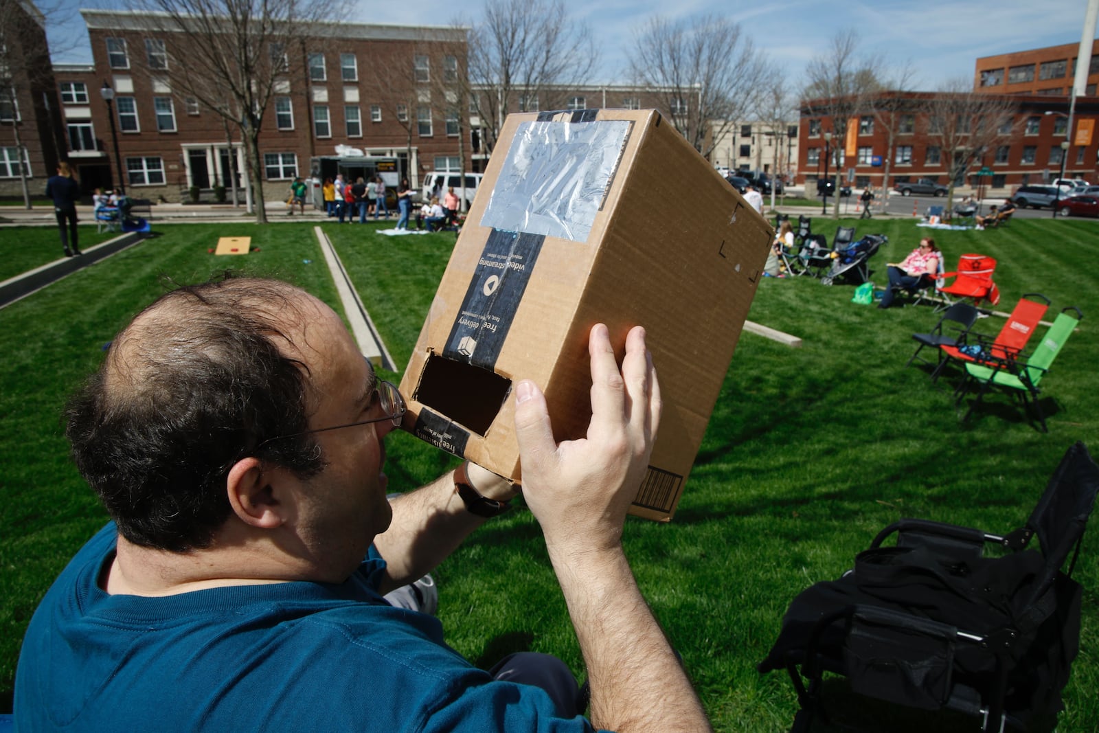 Gary Goldberg, from Maryland, uses a cardboard box with a pin hole to safely view Monday’s eclipse on Monday, April 8, 2024 at National Road Commons. BILL LACKEY / STAFF