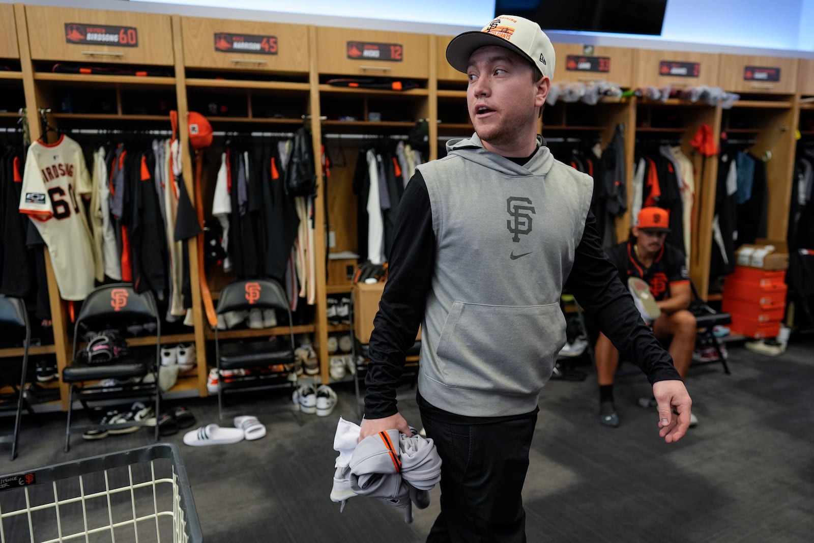 San Francisco Giants clubhouse attendant Riley Halpin gathers dirty clothes in the clubhouse after spring training baseball practice at the team's facility, Monday, Feb. 17, 2025, in Scottsdale, Ariz. (AP Photo/Carolyn Kaster)