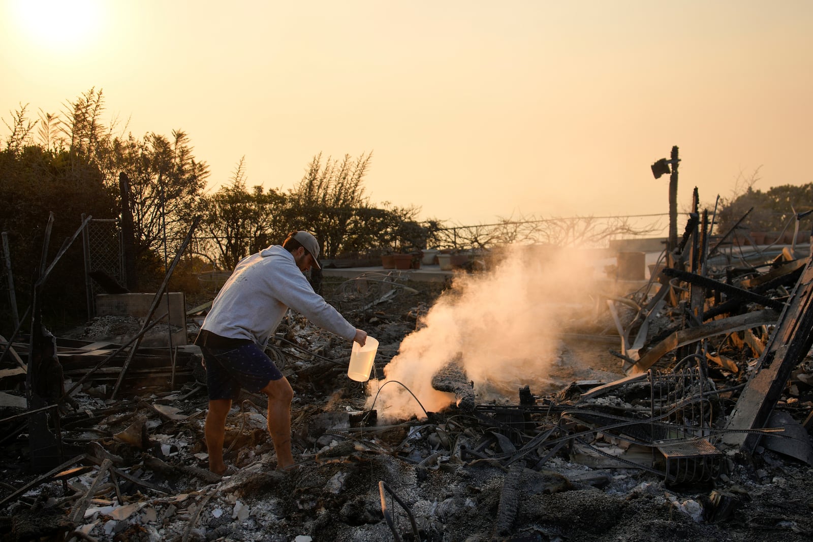 Garrett Yost gathers puts out hotspots with water from a nearby pool while surveying his neighbors' fire-ravaged properties in the aftermath of the Palisades Fire in the Pacific Palisades neighborhood of Los Angeles, Friday, Jan. 10, 2025. (AP Photo/John Locher)