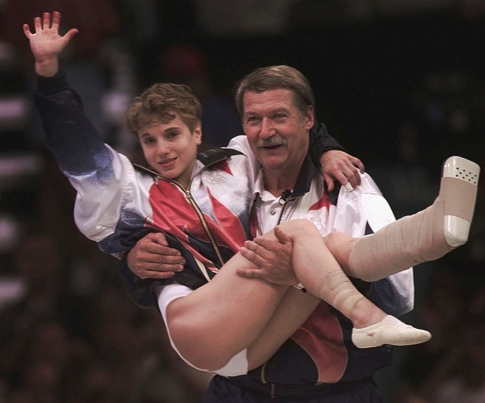 FILE - USA's Kerri Strug is carried by her coach, Bela Karolyi, as she waves to the crowd on her way to receiving her gold medal for the women's team gymnastics competition, at the Centennial Summer Olympic Games in Atlanta, July 23, 1996. Strug had two torn ligaments and a sprained ankle from the vault competition. (AP Photo/Susan Ragan, File)