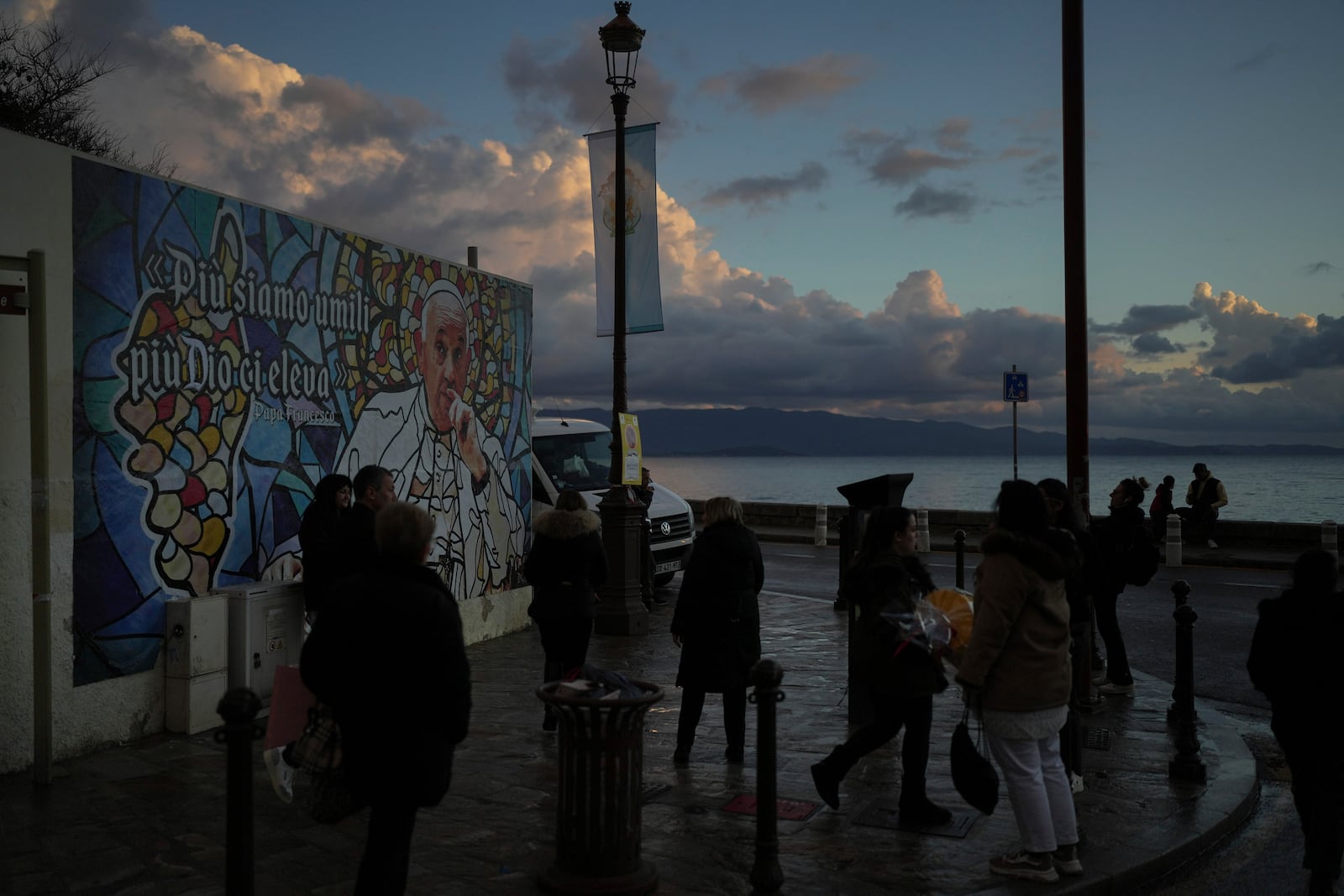 People walk past a mural featuring Pope Francis prior to the Pope's visit, in Ajaccio, in the southern French island of Corsica, Saturday, Dec. 14, 2024. (AP Photo/Thibault Camus)