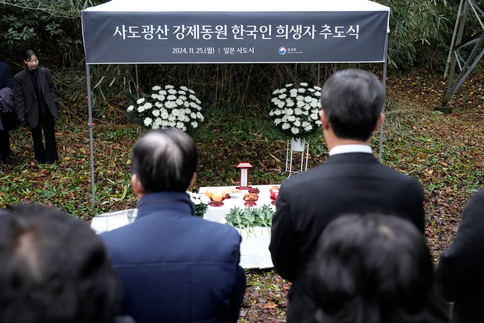 Relatives of Korean victims and South Korean officials offer a prayer during a memorial service at the site of former Fourth Souai Dormitory for the mine workers from the Korean Peninsula, in Sado, Niigata prefecture, Japan, Monday, Nov. 25, 2024, a day after boycotting a memorial organized by Japanese officials. The black banner reads "A memorial service for Korean forced laborer victims at Sado Mine." (AP Photo/Eugene Hoshiko)