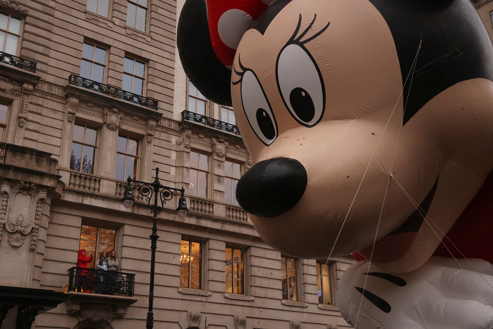 Spectators watch from an apartment balcony as Disney's Minnie Mouse balloon floats by on Central Park West during the Macy's Thanksgiving Day Parade, Thursday, Nov. 28, 2024, in New York. (AP Photo/Yuki Iwamura)