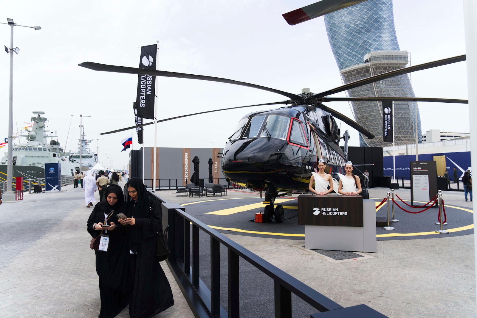 Emirati women walk past a display for Russian Helicopters at the biennial International Defense Exhibition and Conference arms show in Abu Dhabi, United Arab Emirates, Monday, Feb. 17, 2025. (AP Photo/Jon Gambrell)