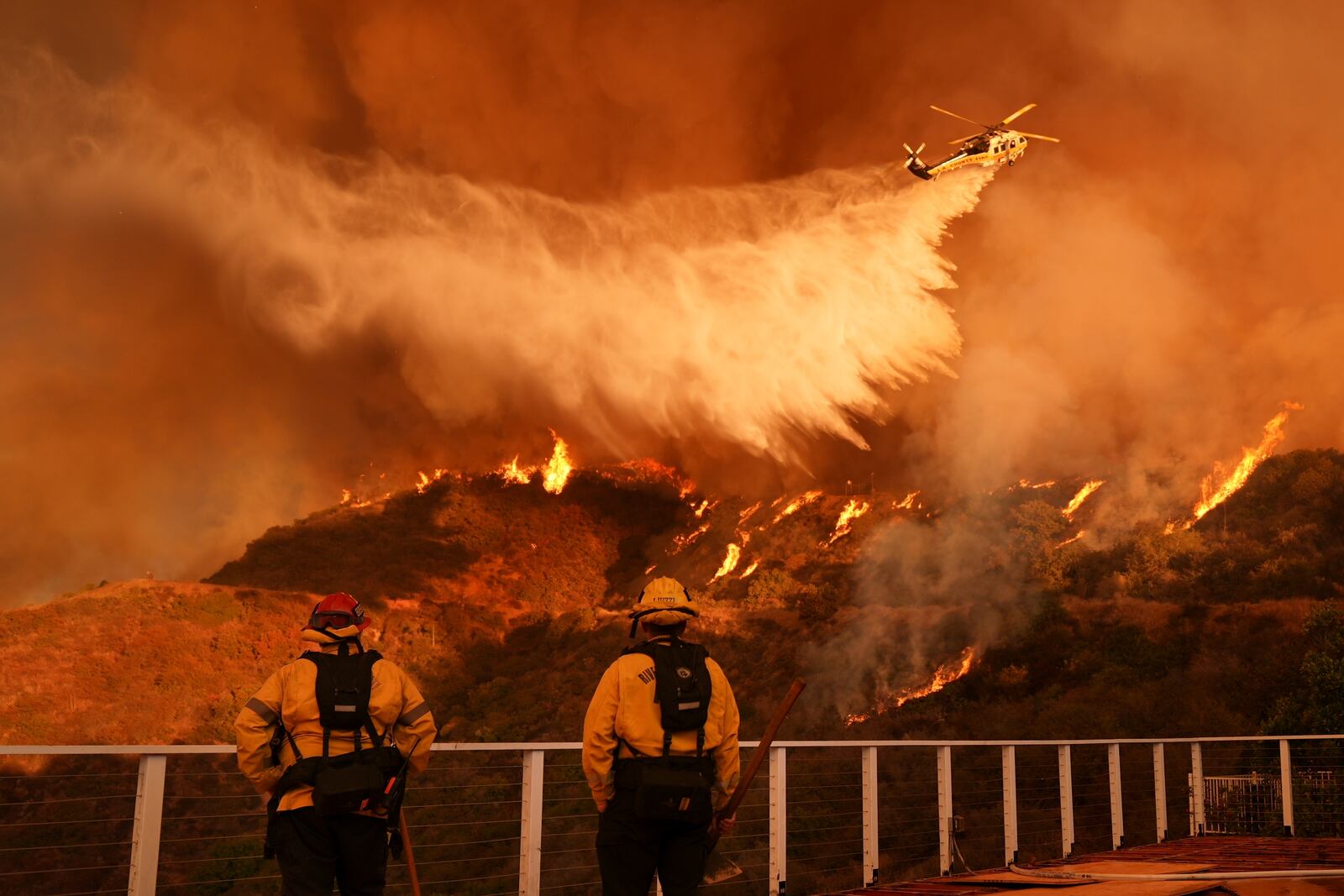 FILE - Firefighters watch a helicopter drop water on the Palisades Fire in Mandeville Canyon in Los Angeles, Jan. 11, 2025. (AP Photo/Jae C. Hong, File)