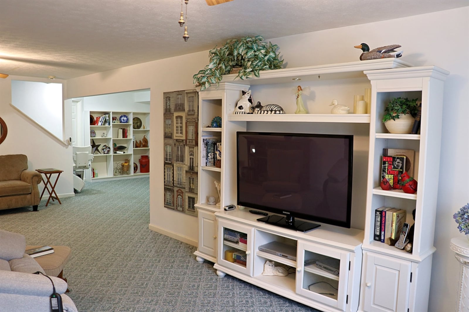 The staircase leads down to the finished lower level. The staircase lands within a sitting room or game area of the larger family room or recreation room. 