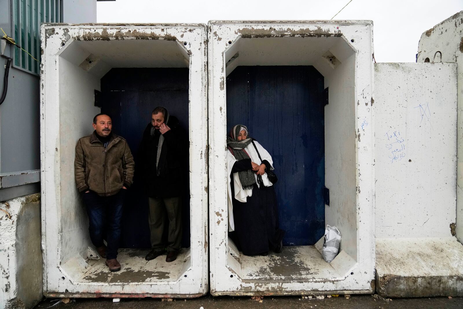 Palestinians take cover from the rain while they try to cross from the Israeli military Qalandia checkpoint near the West Bank city of Ramallah to Jerusalem, to participate in the Friday prayers at the Al-Aqsa Mosque compound during the Muslim holy month of Ramadan on Friday, March 7, 2025. (AP Photo/Nasser Nasser)