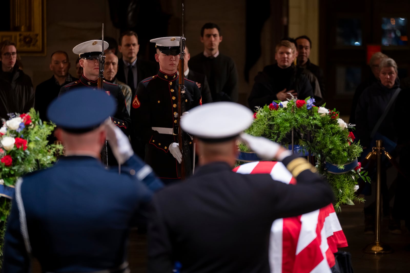 A military honor guard salutes as mourners view the flag-draped casket of former President Jimmy Carter as he lies in state in the Rotunda, at the Capitol in Washington, Tuesday, Jan. 7, 2025. (AP Photo/Ben Curtis)