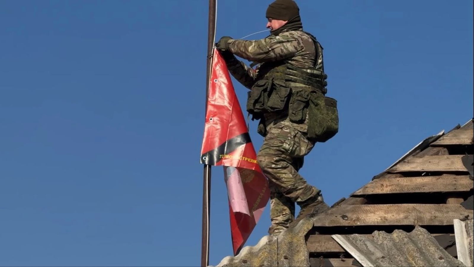 In this photo distributed by Russian Defense Ministry Press Service on Monday, March 17, 2025, a Russian soldier prepares to raise a flag of his unit atop of a house in Staraya Sorochina village in Sudzha district in the Kursk region of Russia after it was taken over by Russian troops. (Russian Defense Ministry Press Service via AP)