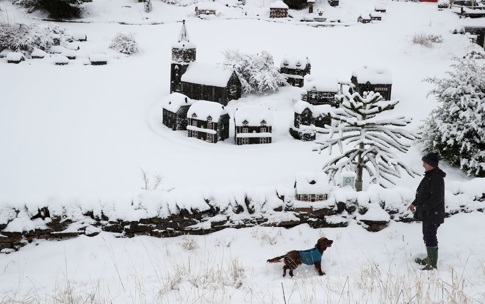 A man walk's his dog in the heavy snow past scaled miniature famous landmarks which are located in Nenthead, England, as the severe weather continues across England, Sunday, Jan. 5, 2025. (AP Photo/Scott Heppell)