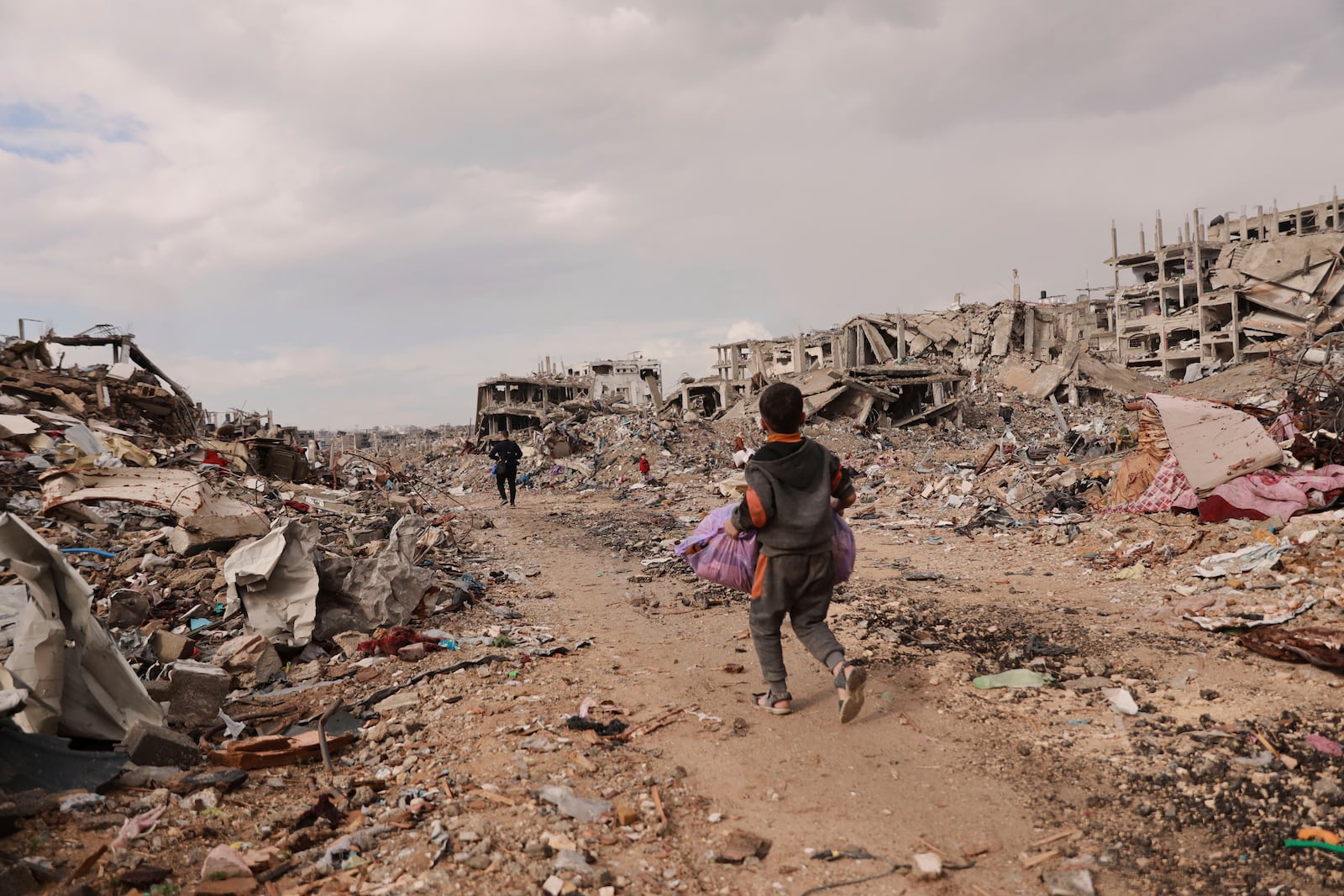 A Palestinian boy carries his belongings as he walks with his family next to the rubble of destroyed homes, after the ceasefire deal between Israel and Hamas, in Gaza City, Gaza Strip, Friday, Jan. 24, 2025. (AP Photo/Abed Hajjar)