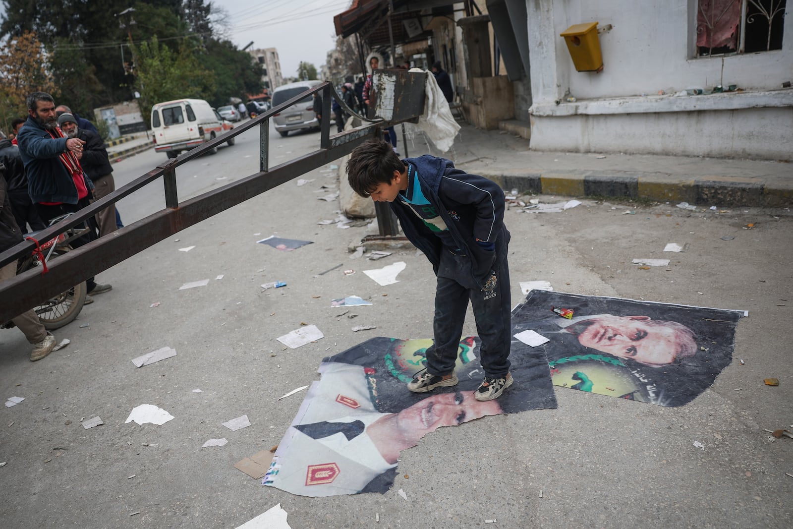 A boy steps over pictures of Syrian President Bashar Assad and his late father, Hafez Assad, right, Salamiyah, east of Hama, Syria, Saturday Dec. 7, 2024. (AP Photo/Ghaith Alsayed)