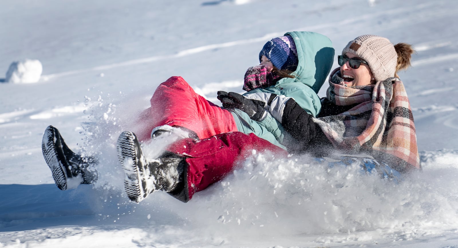 Kristina Foss holds onto her daughter Kayleigh as they plow through snow at the bottom of the hill behind Sherwood Heights Elementary School Auburn, Maine, Monday, Jan. 20, 2025, with family and friends. (Russ Dillingham/Sun Journal via AP)