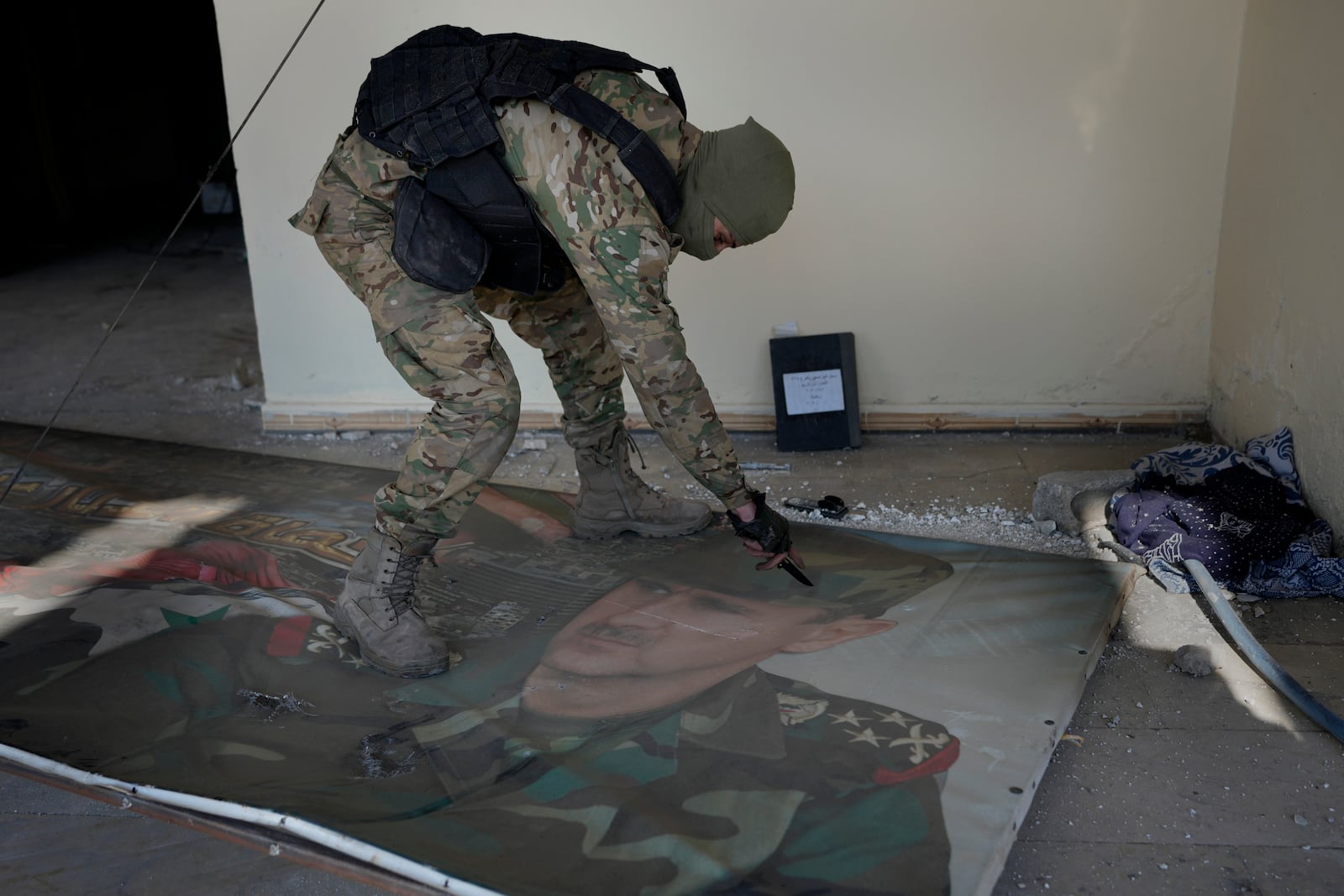 A Syrian fighter from rebel group, uses his knife to tear a poster at the entrance to the notorious security detention centre called Palestine Branch, which shows the ouster Syrian President Bashar Assad in Damascus, Syria, Saturday, Dec. 14, 2024. (AP Photo/Hussein Malla)