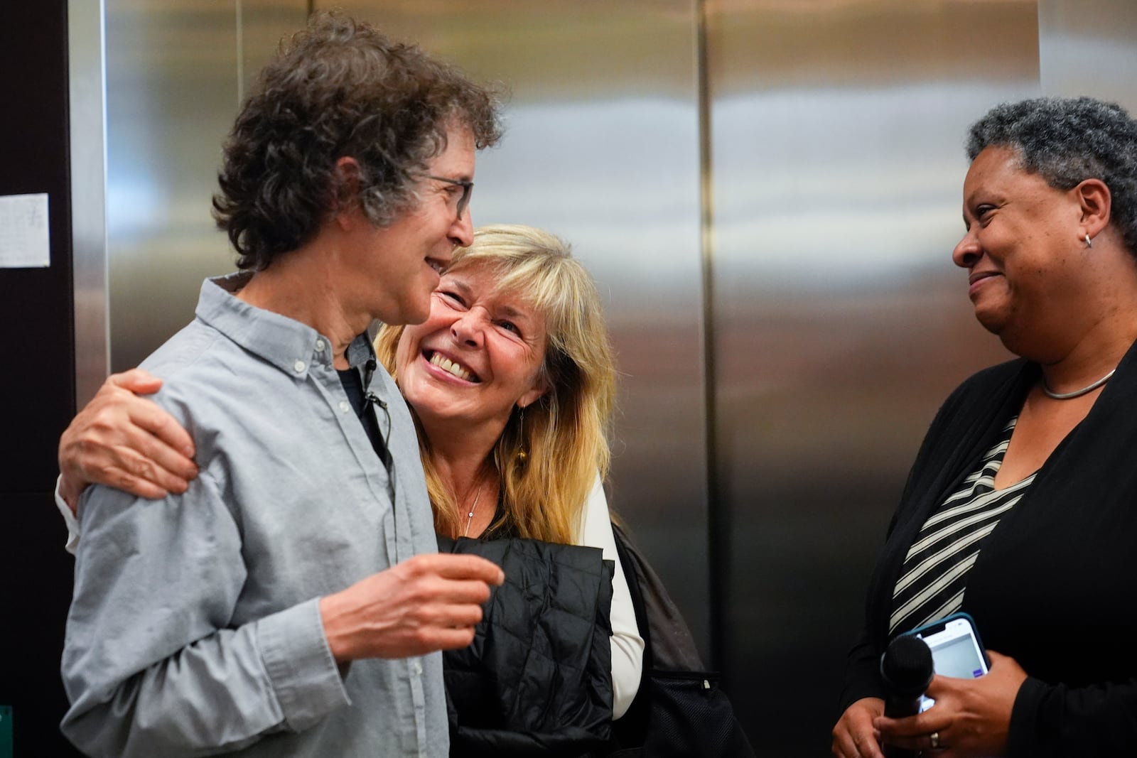 Hannele Ruohola-Baker hugs her husband American biochemist David Baker, 2024 Nobel Prize winner in Chemistry, at the University of Washington on Wednesday, Oct. 9, 2024, in Seattle. Lynda Stuart, executive director at the Institute for Protein Design, looks on at right. (AP Photo/Lindsey Wasson)