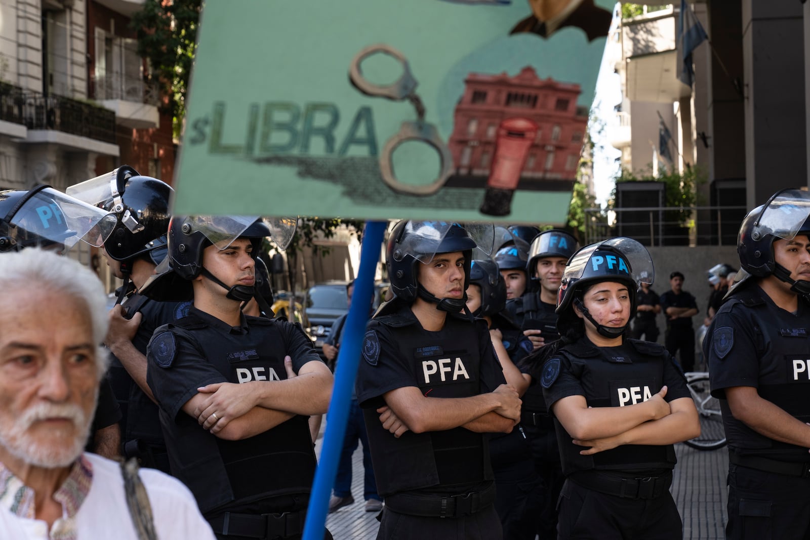 Riot police stand guard as a demonstrator holds a banner depicting the $Libra cryptocurrency during a protest organized by retirees demanding better pensions, in Buenos Aires, Argentina, Wednesday, Feb. 19, 2025. (AP Photo/Rodrigo Abd)