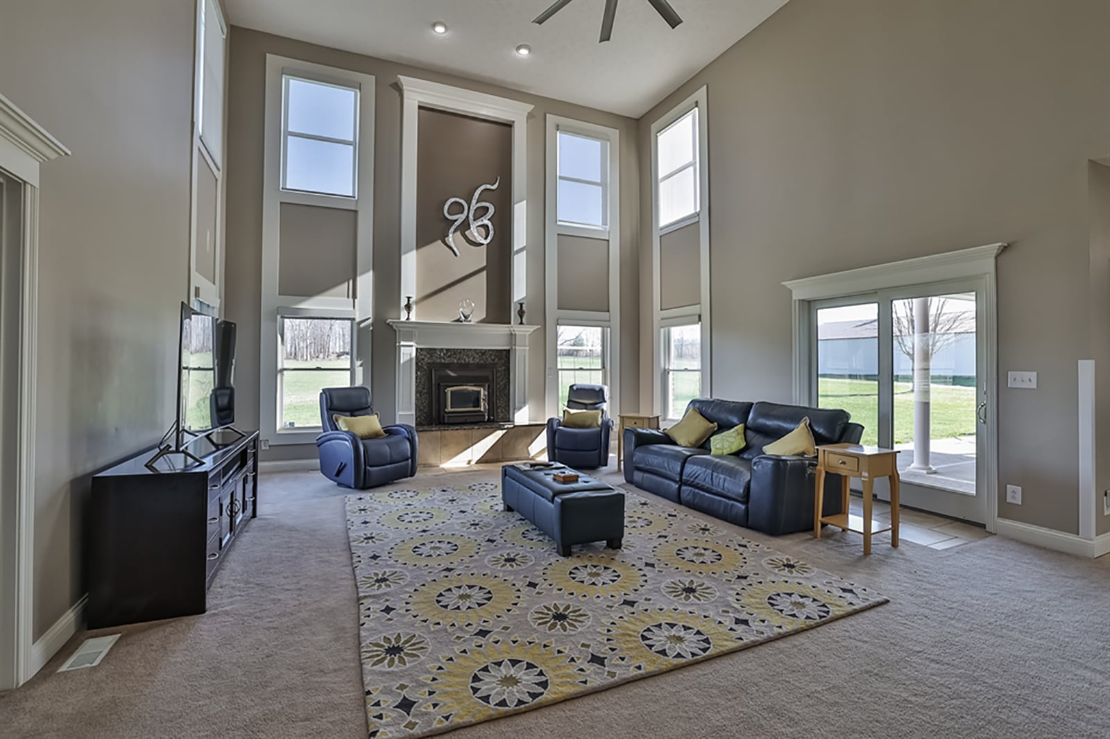 The great room has a 2-story ceiling with recessed lights and ceiling paddle fan. A gas fireplace has a double wooden mantle that extends to near ceiling height. Windows are stacked on each side of the fireplace and within the corners. CONTRIBUTED PHOTO