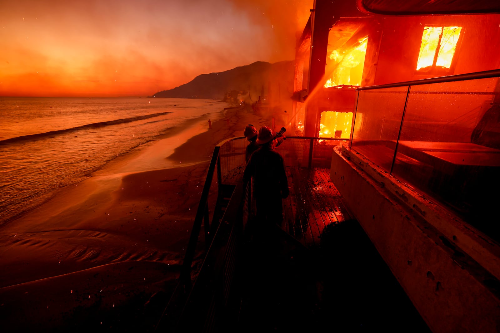 FILE - Firefighters work from a deck as the Palisades Fire burns a beachfront property Wednesday, Jan. 8, 2025 in Malibu, Calif. (AP Photo/Etienne Laurent, File)