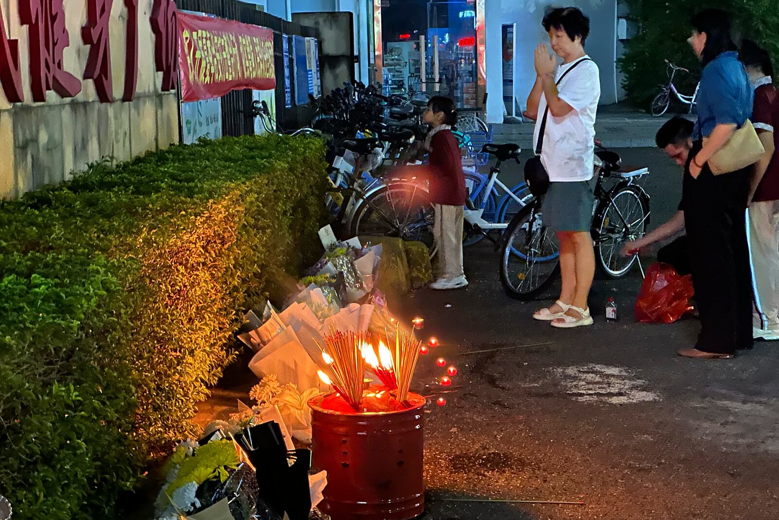 A woman prays after incense were offered near flowers places outside the "Zhuhai People's Fitness Plaza" where a man deliberately rammed his car into people exercising at the sports center, killing some and injuring others in Zhuhai in southern China's Guangdong province on Tuesday, Nov. 12, 2024. (AP Photo/Ng Han Guan)