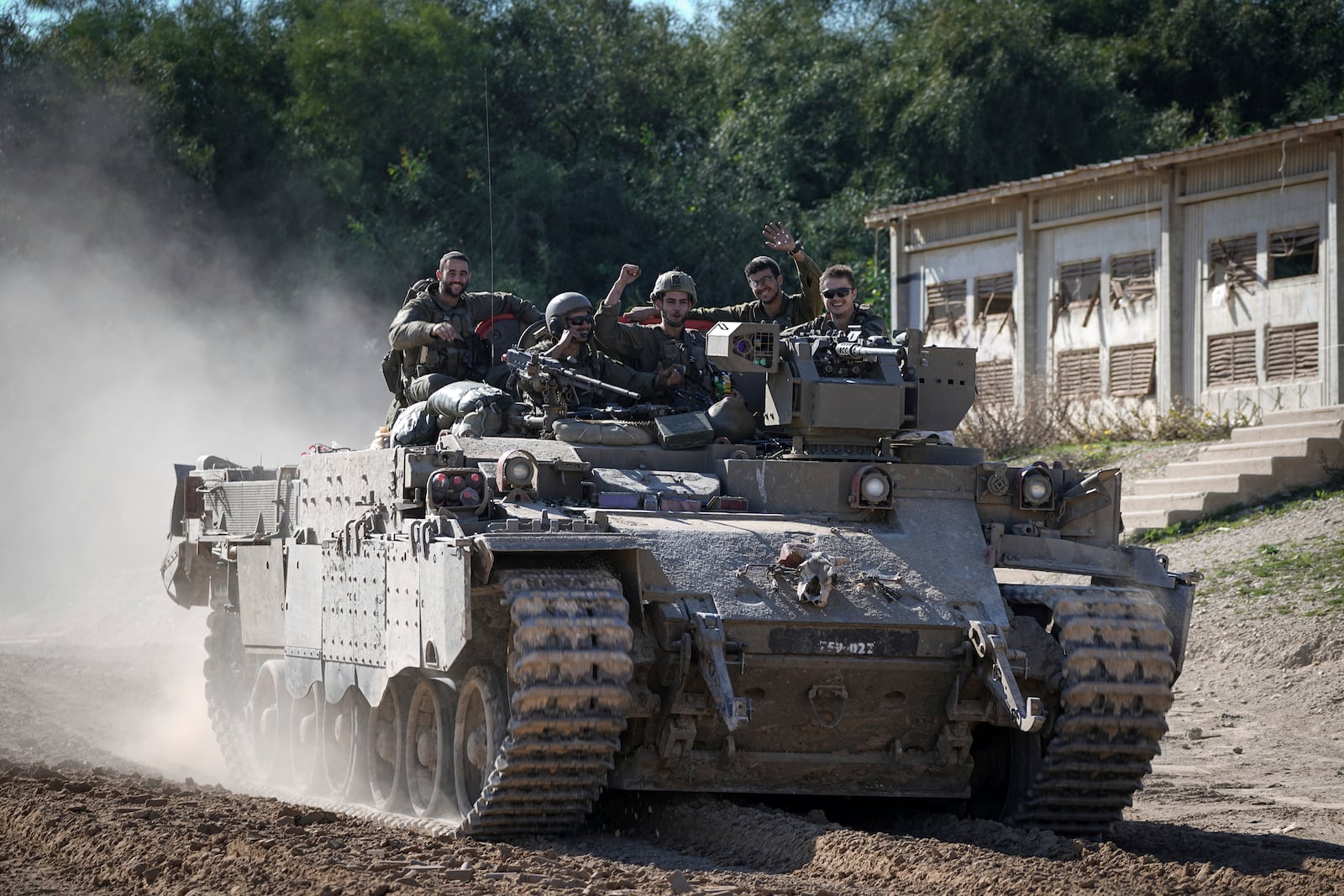 Israeli soldiers wave to the camera from an APC as they cross from the Gaza Strip into Israel, Saturday, Jan. 18, 2025. (AP Photo/Tsafrir Abayov)