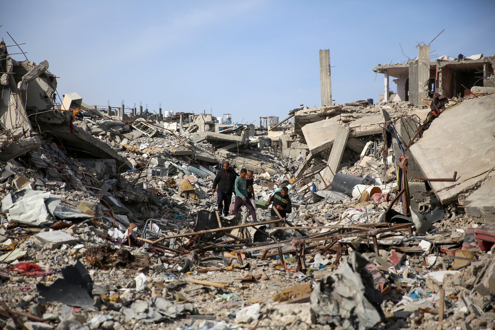 Palestinians walk through the destruction caused by the Israeli air and ground offensive in Rafah, as a ceasefire deal between Israel and Hamas went into effect, Sunday, Jan. 19, 2025. (AP Photo/Mohammad Hajjar)